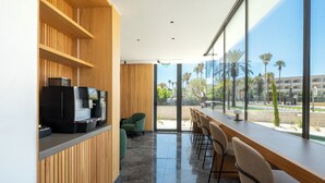 Een moderne bar met een houten toonbank, zitplaatsen en een groot raam met uitzicht op palmbomen en gebouwen.