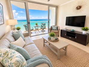 Sala de estar com sofá, mesa de centro, televisão e varanda com vista para o mar.