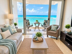 A living room with a sofa, armchair, and coffee table, a small table with plants, and a view of the ocean through large glass doors. - Beachfront * Washer/D * Walk 2 eat (Carolina)