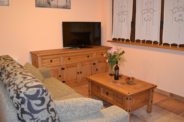 Un salón con sofá, mueble de madera, televisión y una mesa con un jarrón y copas de vino.