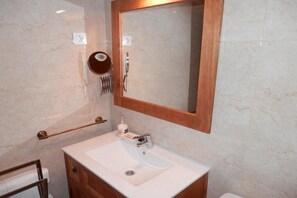 Un baño con lavamanos de mármol, tocador de madera y espejo con marco de madera.