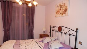 Ein Schlafzimmer mit Bett, Vorhängen, einem Nachttisch mit Lampe und einem Wandbild.