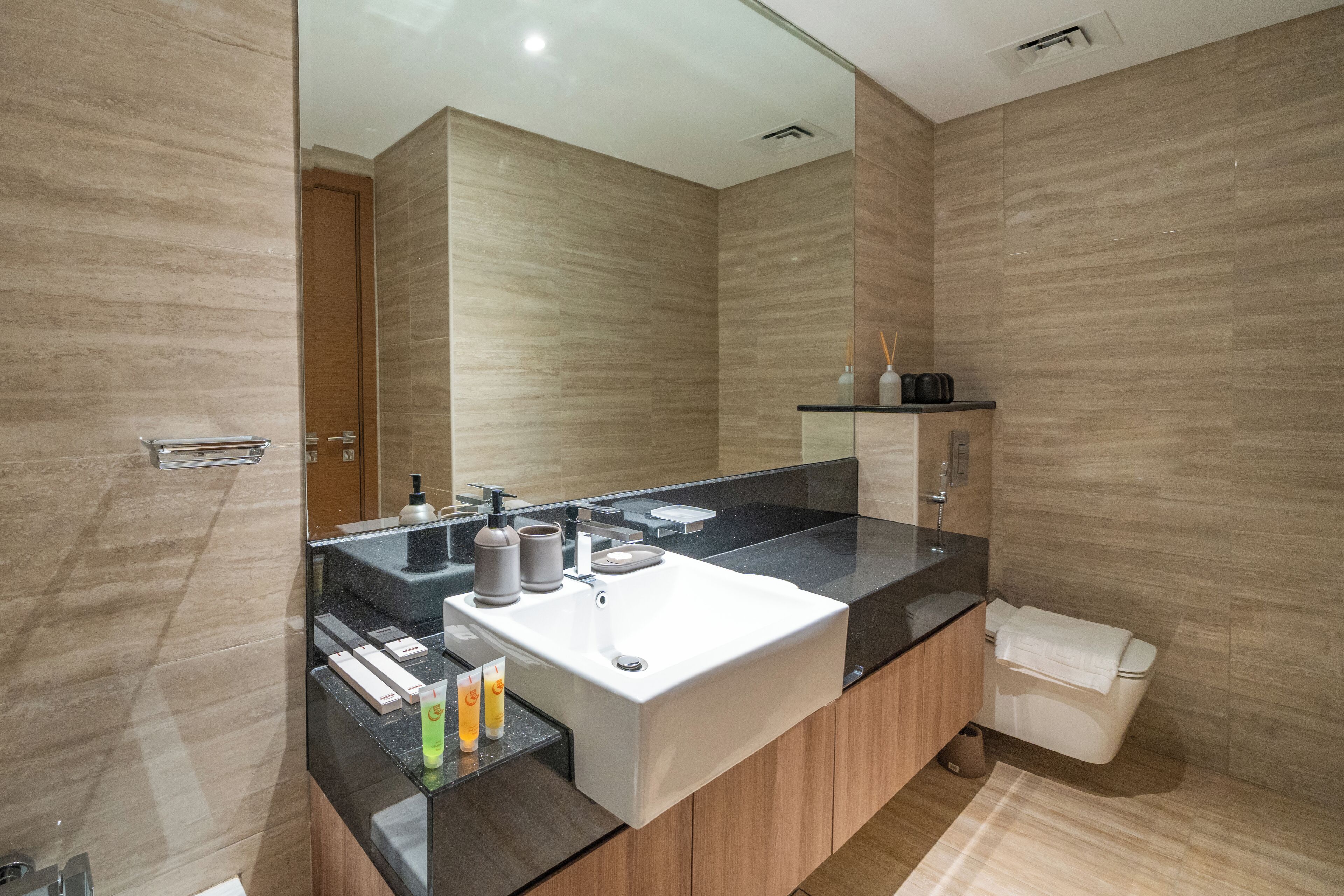 A modern bathroom with a large mirror, a black countertop, a white sink, and wooden cabinets.