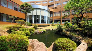 Un bâtiment moderne doté d’une cour intérieure agrémentée d’un bassin, de rochers et d’arbustes soigneusement taillés.