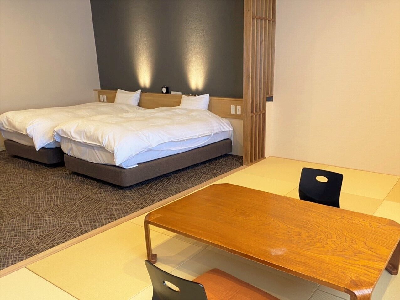 A hotel room with two beds, a wooden table, and a chair.