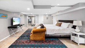 A modern hotel room with a large bed, a desk with a TV, a sofa, and a patterned rug. - Clarendon Getaway, 6-BR Luxurious Urban Estate (Arlington)