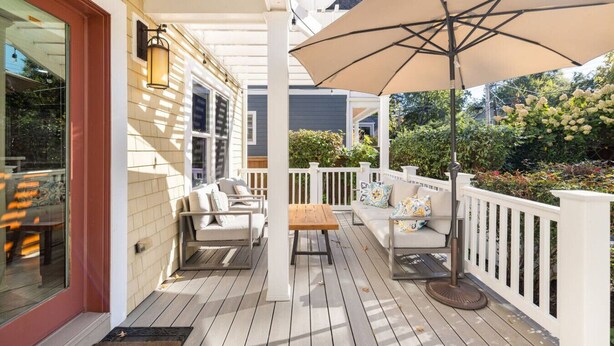 A covered porch with outdoor furniture, a wooden table, and a large umbrella. - Clarendon Getaway, 6-BR Luxurious Urban Estate (Arlington)