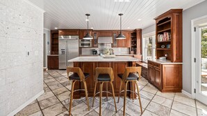 A modern kitchen with a central island, wooden bar stools, and built-in wooden cabinets. - Clarendon Getaway, 6-BR Luxurious Urban Estate (Arlington)