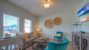 A living room with a sofa, teal armchairs, a coffee table, and a dining area with chairs and a table.