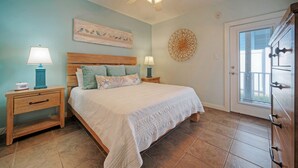 A bedroom with a bed, nightstands, a ceiling fan, and a door leading to a balcony.