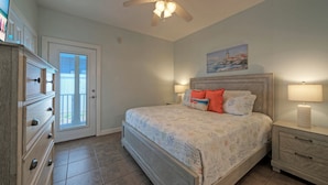 A bedroom with a bed, nightstands, a dresser, a ceiling fan, and a door with a view.