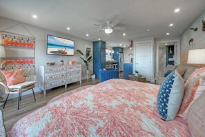 A bedroom with a large bed, a ceiling fan, a dining area, and a bathroom visible through an open door.