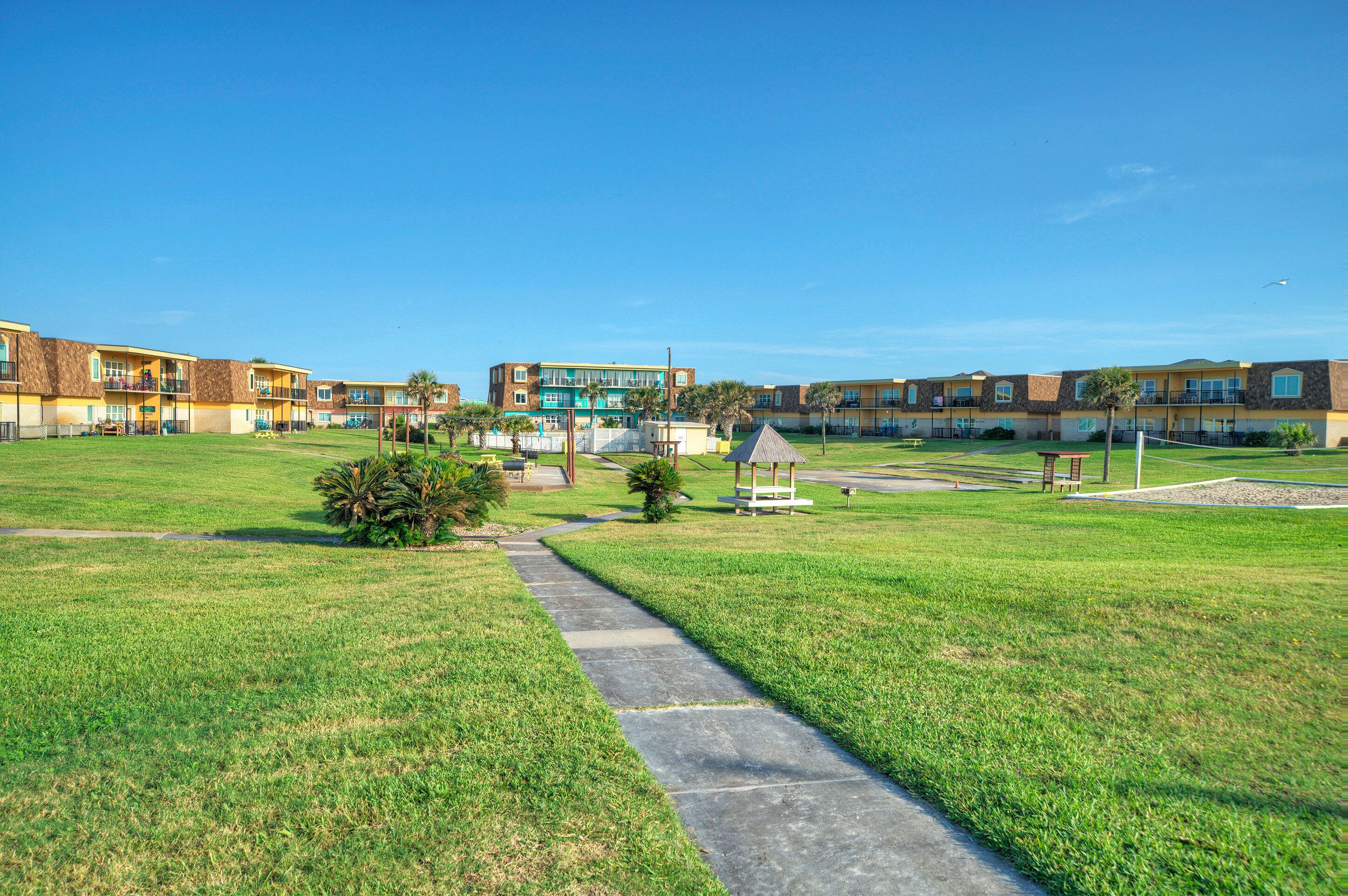 A hotel with multiple-story buildings, a grassy courtyard, and a clear blue sky.