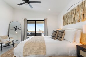 A bedroom with a bed, a ceiling fan, a large mirror, a chair, and a view through a glass door.