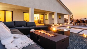 An outdoor living area with a sofa, a fire feature, and a dining setup. - Bocce, Pool+Spa, Game Room, Firepit | Modern Oasis | Yucca Haven by AvantStay (Yucca Valley)