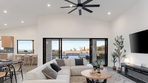 A modern living room with a sectional sofa, a round coffee table, and a dining area with a wooden table and chairs. - Bocce, Pool+Spa, Game Room, Firepit | Modern Oasis | Yucca Haven by AvantStay (Yucca Valley)