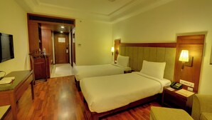 Ein Hotelzimmer mit zwei Betten, Holzboden, einem Schreibtisch, einem Stuhl, einem Fernseher und einem Deckenventilator.