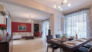 A modern living room with a dining area, featuring a sofa set, a dining table set for four, and a chandelier.