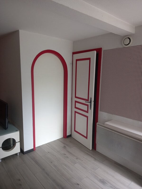 A room with a white door with red trim, a white cabinet with a black object on top, and a white sink with a perforated panel above it. - Garden level (Gap)