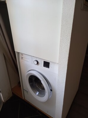A front-loading washing machine in a laundry room with a control panel and a small display.