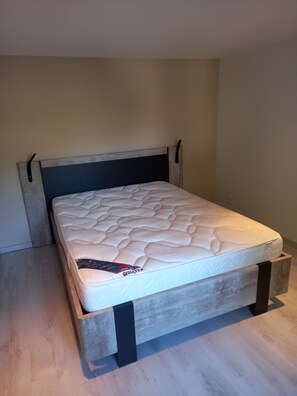 A bed with a wooden frame and a headboard, a mattress with a white cover, and a wooden floor.