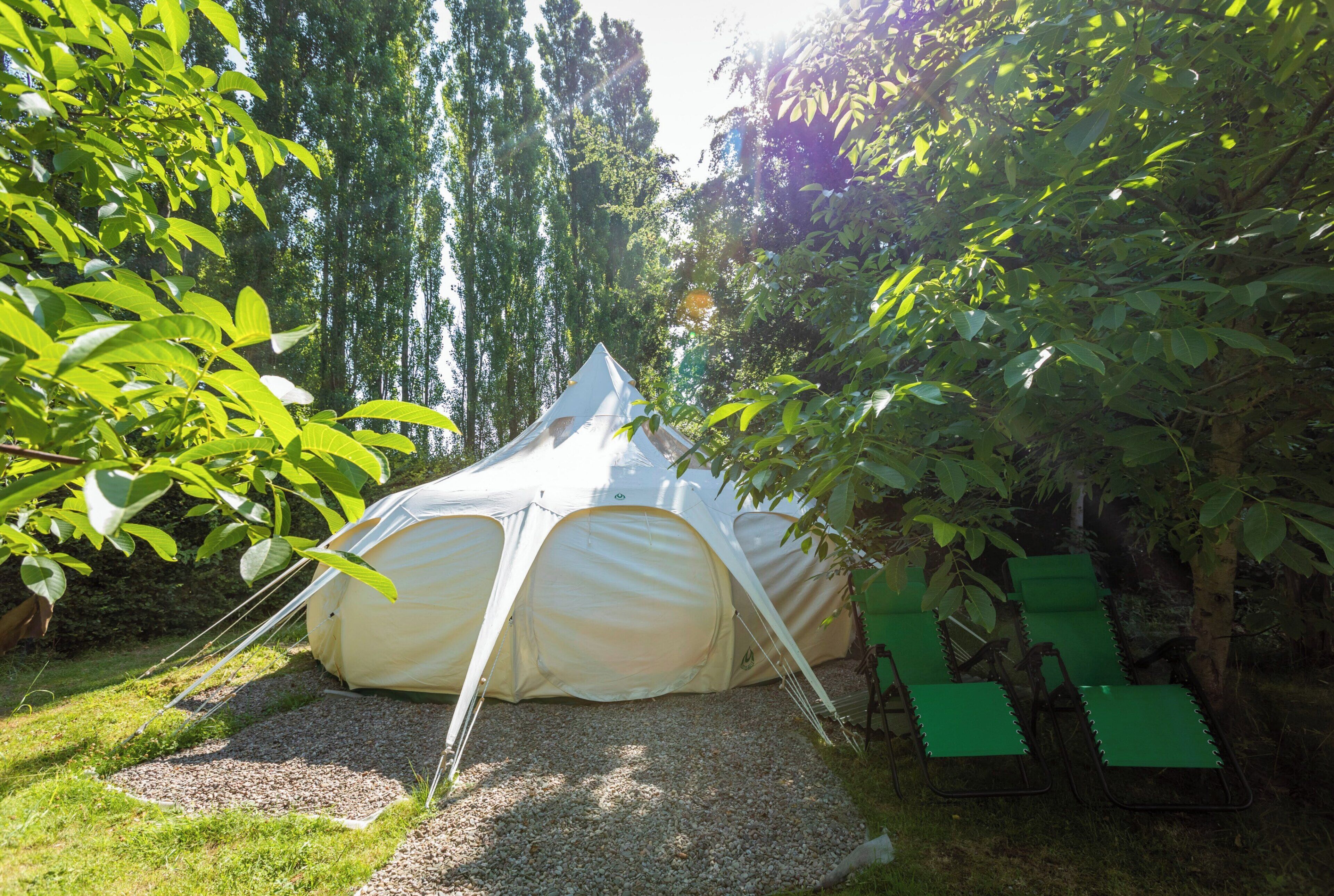 Ein Zelt ist in einem Garten aufgebaut, mit einem Kiesweg, der dorthin führt, umgeben von üppigem Grün und Bäumen.