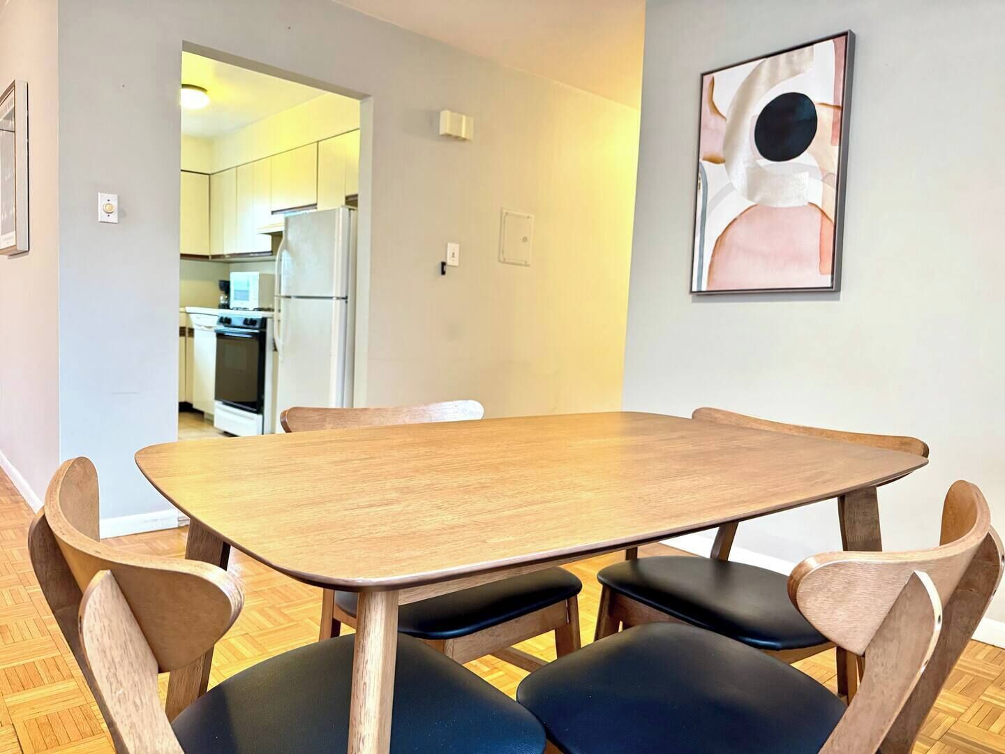 Ein Essbereich mit Holztisch und Stühlen, eine Küche im Hintergrund und ein gerahmtes abstraktes Gemälde an der Wand.