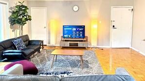 A living room with a sofa, coffee table, and TV. There is a plant, a clock, and two doors.