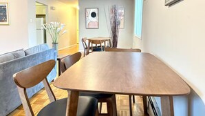 A dining area with a wooden table and chairs, a sofa, and a vase of white flowers.