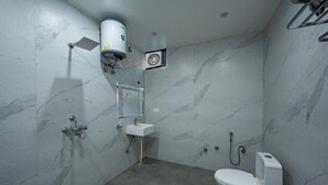 Un baño con piso de mármol, lavamanos blanco, inodoro y zona de ducha.