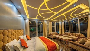 Habitación de hotel con una cama grande, un sofá y una mesa de centro. Hay cortinas en las ventanas y el diseño de la habitación es moderno.