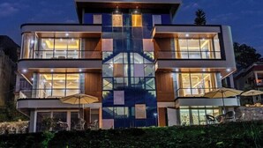 Un edificio moderno de dos pisos con grandes ventanales, asientos al aire libre y una escalera central.