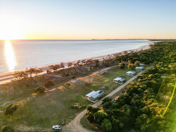 An aerial view of a coastal property with a beach, a dirt road, and several buildings.