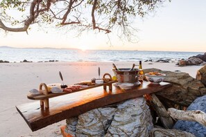 A wooden bar set on a rocky beach with a sunset view.