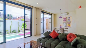 A modern living room with a green sofa, a coffee table, and a dining area with a small table and chairs. - Stylish Private Pool Villa in Pererenan (Munggu)