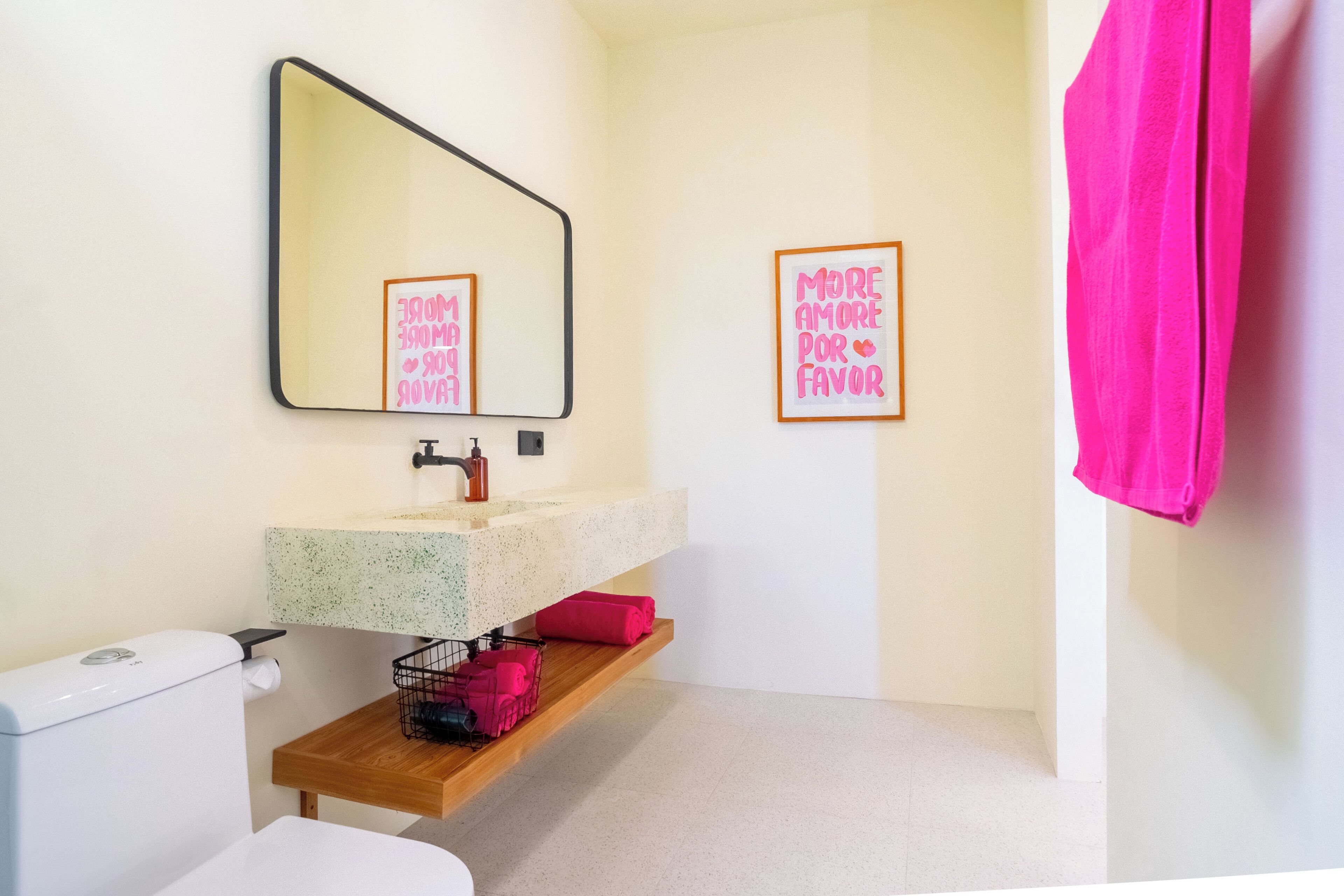 Un bagno con il water, un lavandino, uno specchio e uno scaffale con un asciugamano rosa.
