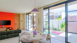 A modern living room with a large TV, green sofa, and a dining area with a table set for four. - Stylish Private Pool Villa in Pererenan (Munggu)