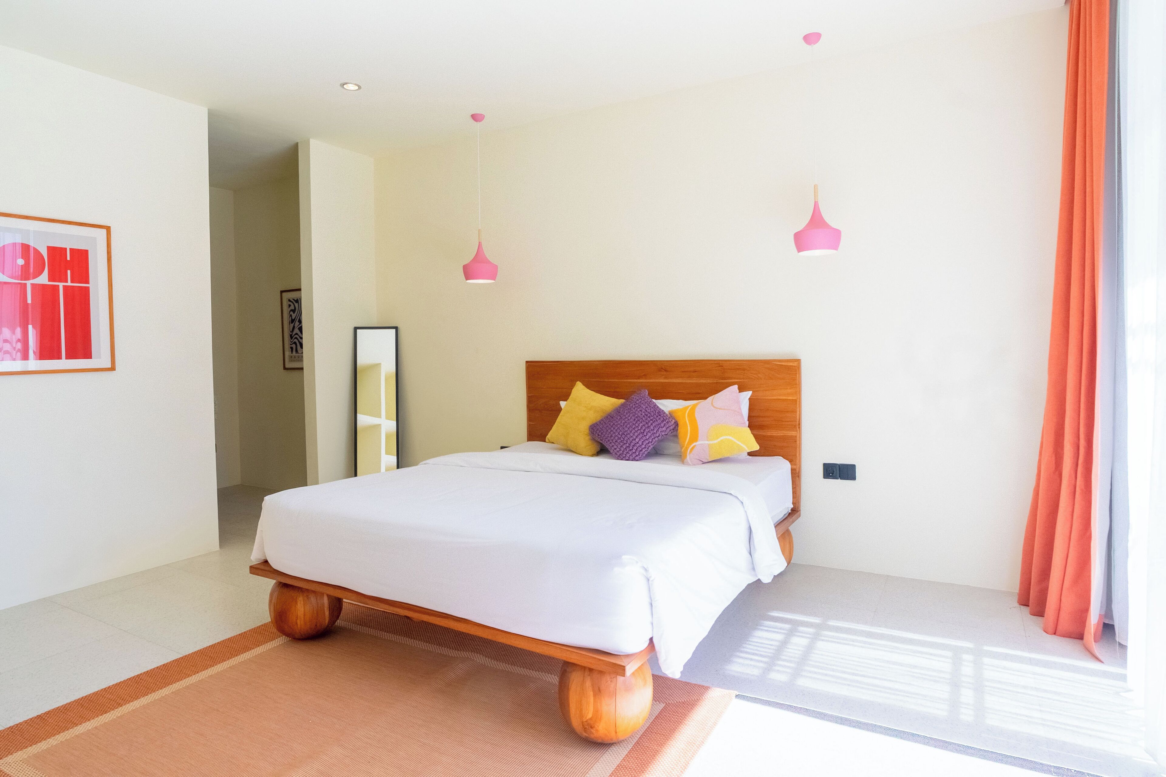 A bedroom with a wooden bed frame, white bedding, and colorful pillows.