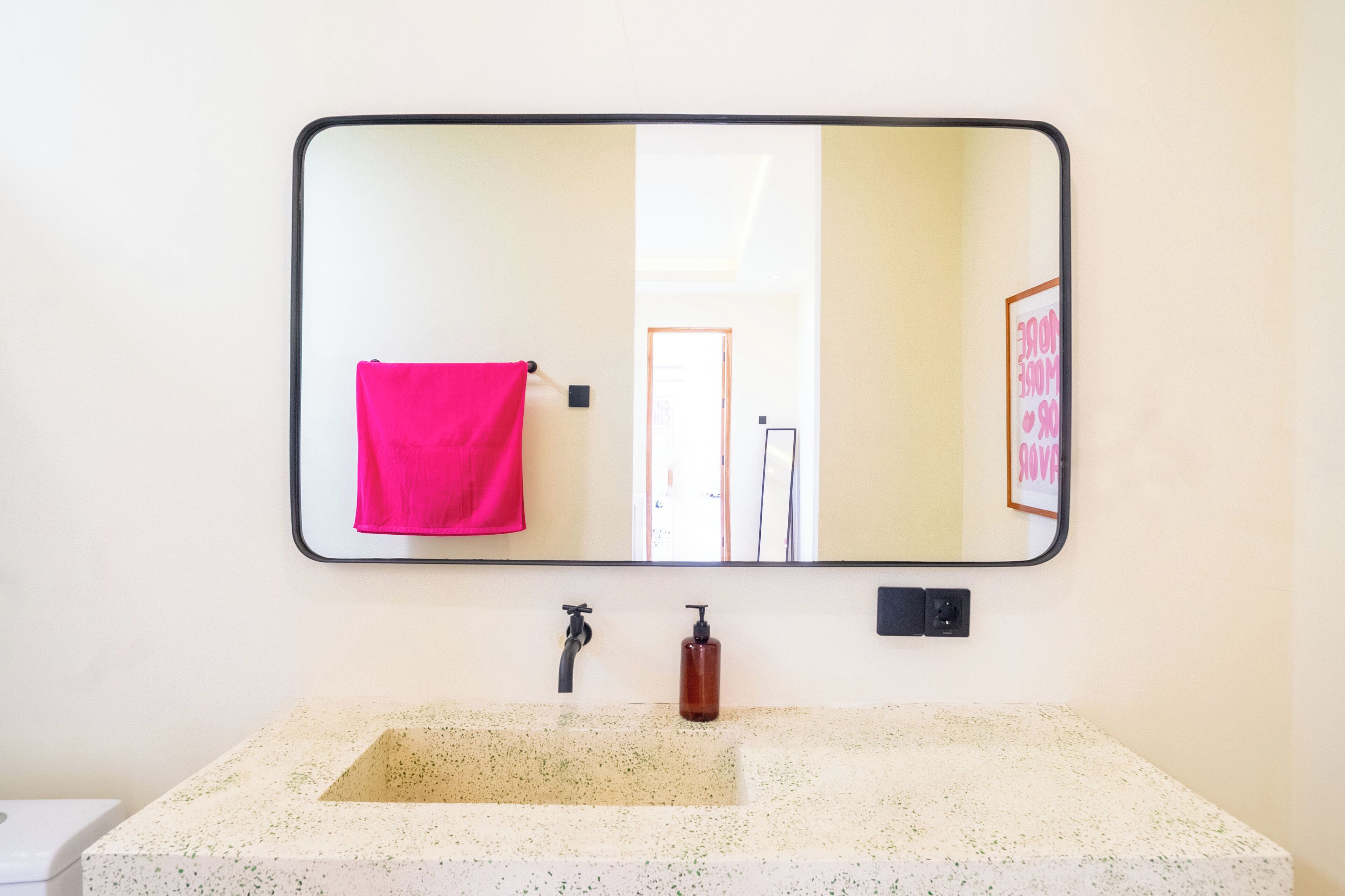 Une salle de bain avec un grand miroir, un lavabo, une serviette rose et un distributeur de savon.