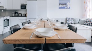 A modern kitchen with white cabinets, a wooden dining table set for six, and a sofa with patterned cushions.