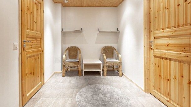 A room with wooden-paneled walls, two wicker chairs, a small table, and a round rug.