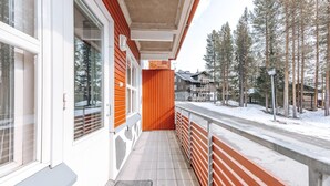 A covered outdoor area with a wooden railing, a snow-covered ground, and a view of a residential area with houses and trees.