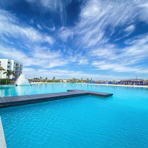 Un ciel bleu azur parsemé de nuages, une piscine avec une terrasse en bois et un bâtiment doté de balcons.