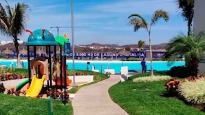 A pathway leading to a playground with a slide, surrounded by well-maintained grass and palm trees. - Apartment with an artificial beach! (Mazatlán)