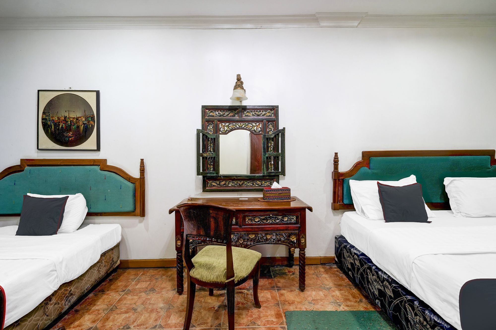 A hotel room with two beds, a wooden desk, a chair, a mirror, and a framed picture on the wall.
