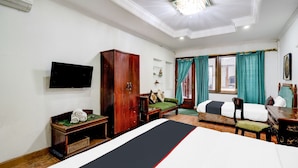 A hotel room with a bed, a wardrobe, a television, a desk with a chair, and a window with curtains.