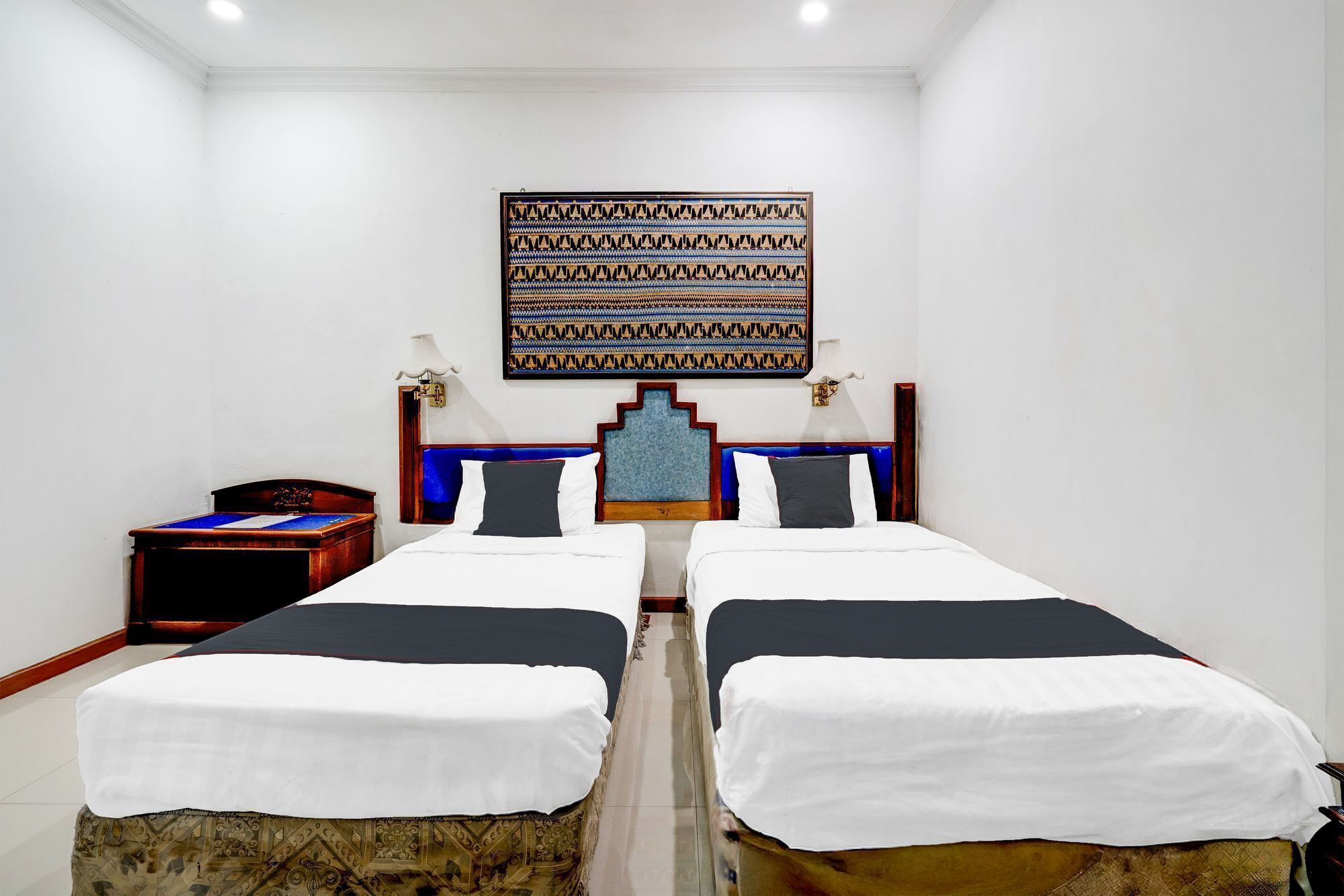 Habitación de hotel con dos camas individuales, una mesita de noche, una lámpara fijada a la pared y un adorno colgante.