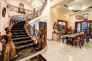 A grand staircase with ornate railings and a chandelier, leading to a dining area with wooden furniture and a view of the outdoors. - Hotel O Bandung near Stadion Siliwangi formerly The Ethnic Hotel Bandung (Bandung)