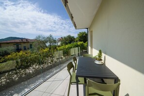 A balcony with a table and chairs, overlooking a garden and a building in the background. - Domus Garda Relax (Garda)