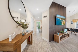 A hotel reception area with a wooden reception desk, a large mirror, a flat-screen TV mounted on the wall, and a view of the sea through the window.